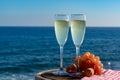 Champagne, prosecco or cava served with pink grape in two glasses on outside terrace with sea view