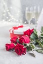 Champagne and red roses with bokeh. Valentine`s setting with red roses and present Royalty Free Stock Photo