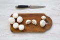 Champignon mushrooms on wooden board with knife over white wooden background, top view. Royalty Free Stock Photo