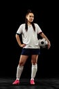 Full-length portrait of sportive girl, female soccer, football player posing on black studio background. Sport