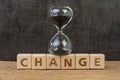 Change, transform or evolve concept, sand glass or hourglass on cube block with alphabet building the word Change on wood table