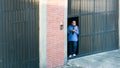 Middle aged male security guard standing at big black door of warehouse; phone in hands.