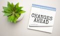 Changes Ahead is written in a white notepad near a clipboard, calculator, green plant, glasses and a pen on a yellow and concrete Royalty Free Stock Photo