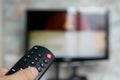 Changing TV program: close up of human hand holding television remote control on blured background with TV screen Royalty Free Stock Photo