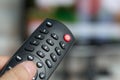 Changing TV program: close up of human hand holding television remote control on blured background with TV screen Royalty Free Stock Photo