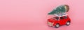 Changxing, China - October 15, 2019: Red toy car with a christmas tree on the roof on pink paper background. Winter delivery, xmas Royalty Free Stock Photo