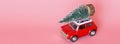 Changxing, China - October 15, 2019: Red toy car with a christmas tree on the roof on pink paper background. Winter delivery, xmas Royalty Free Stock Photo