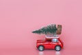 Changxing, China - October 15, 2019: Red toy car with a christmas tree on the roof on pink paper background. Winter delivery, xmas Royalty Free Stock Photo