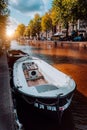 Channel in Amsterdam at autumn sunset. Boat in front of tree-lined canal, white clouds in the sky. Netherlands houses landmark Royalty Free Stock Photo