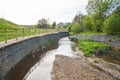 A channel made of granite stones for the river stream with grass and shrubs on the banks. Landscaping of the city, river