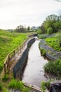 A channel made of granite stones for the river stream with grass and shrubs on the banks. Landscaping of the city, river