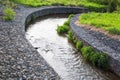 A channel made of granite stones for the river stream with grass and shrubs on the banks. Landscaping of the city, river