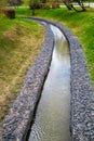 A channel made of granite stones for a stream of a river with green grass on the banks in a city park. Landscaping