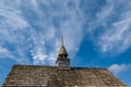 Chapel old wood tiles roof top with steeple against bold blue sky and moving white clouds