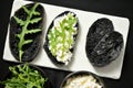 Charcoal black rye bread with cottage cheese and rocket on a black background