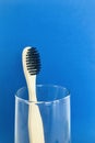 Charcoal infused bamboo toothbrush in glass on navy blue background. Vertical.