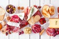 Charcuterie board of assorted cheeses, meats and appetizers, above view table scene over white wood Royalty Free Stock Photo