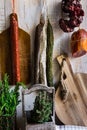 Charcuterie, variety of sausages hanging on hook, wood cutting board, string with dry peppers, fresh garden herbs, Provence