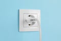 Charger adapter plugged into power socket on light blue wall. Electrical supply Royalty Free Stock Photo