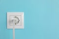 Charger adapter plugged into power socket on light blue wall, space for text. Electrical supply Royalty Free Stock Photo