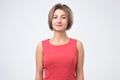 Charismatic attractive woman in red dress, smiling cheerfully while standing against gray background