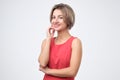 Charismatic attractive woman in red dress, smiling cheerfully while standing against gray background