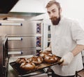 Charismatic baker holds the baking tray with newly-baked bread in the bakery