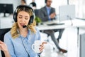 Opearator woman in headset and holding coffee cup talking with customer during online phone call at helpdesk office. Royalty Free Stock Photo