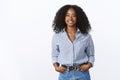 Charismatic cheerful attractive african american woman curly haircut wearing shirt holding hands pockets confident