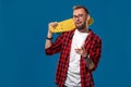 Charismatic cheerful young bearded man dressed in checkered shirt, white T-shirt and glasses, with yellow skateboard in