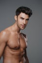 Close-up portrait of a sexy brunette male model with a bare torso against a gray background