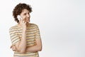 Charismatic curly guy talking on mobile, having phone call and smiling, standing in t-shirt over white background