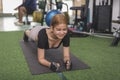 A charismatic woman smiles while doing planks on a black mat. Having fun and a lighthearted moment at the gym