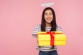Charity and donations. Portrait of angelic asian girl with halo over head giving gift box to camera and modestly smiling