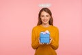 Charity and human kindness. Portrait of angelic ginger girl with halo over head holding gift box and smiling at camera, sharing