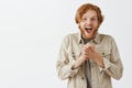 Charmed and thrilled expressive redhead male fan in outdoor jacket clenching palms near chest gasping and dropping jaw