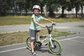 Active Caucasian child boy, in sports helmet, looking at camera, standing near his bicycle on the asphalt road outdoor.