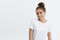 Charming adult caucasian woman with bun smiling broadly and glancing at camera, standing against white background. Cute