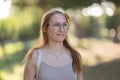 Charming adult woman in glasses with dyed red hair standing in the park looking forwards Royalty Free Stock Photo