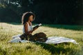 Charming african girl with natural make-up and curly hair is relaxing with the book during the picnic on the sunny