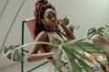 Charming African woman, wearing a multicolor ornament dress, sitting in a hammock chair surrounded by tropical plants. Resting in