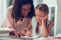 Charming Afro-American mother helping her sweet schoolkid with a homework.