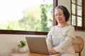 Charming aged Asian female entrepreneur remote working at home, using laptop computer Royalty Free Stock Photo