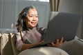 Charming asian aged woman relaxes, leaning sits on sofa and using laptop