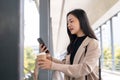 A charming Asian businesswoman chatting on her smartphone while having a quick coffee break outdoors