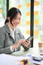 Charming Asian businesswoman or female office worker using her smartphone at her desk Royalty Free Stock Photo