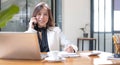 Charming Asian businesswoman working with a laptop and use smartphone at the office. Looking at camera. Royalty Free Stock Photo