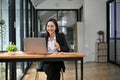 Charming Asian businesswoman working on a project at her desk, using laptop while sipping coffee Royalty Free Stock Photo