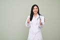 Charming Asian female doctor showing thump up, holding a smartphone mockup