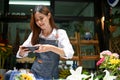 Charming Asian female florist photographing flower arrangement with her mobile phone